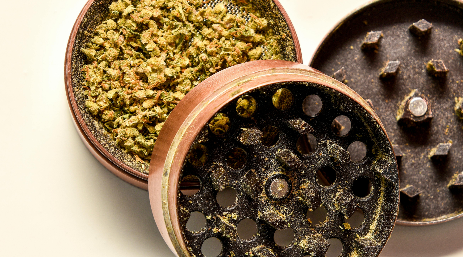 Close-up of a weed grinder filled with freshly ground cannabis, showing the teeth, pollen chamber, and plant material buildup.
