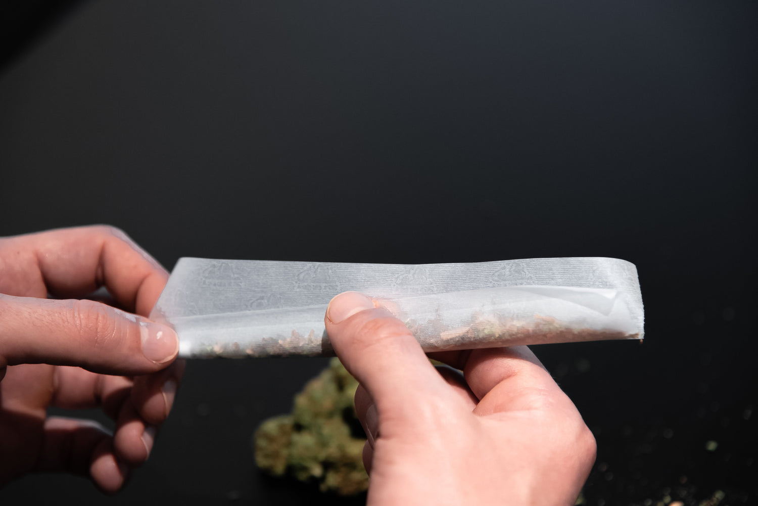 Hands preparing a roll using hemp-based rolling paper filled with herbal blend