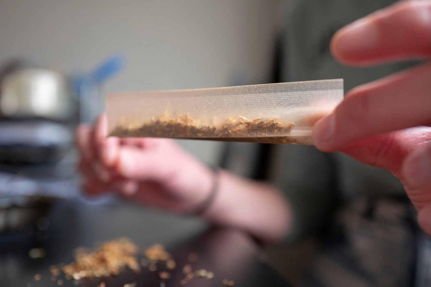 Close-up of hands rolling shredded tobacco into a cigarette with thin, unbleached paper, representing the choice between organic and traditional rolling papers for a healthier, more sustainable smoking experience.