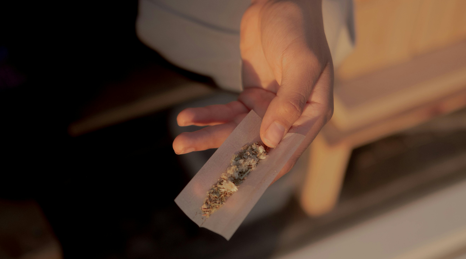 Hand holding a partially filled rolling paper during golden hour, showing the process of choosing the best rolling papers for joint quality and consistency.